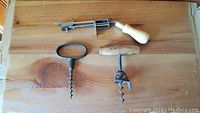 All four items displayed on a wooden surface, showing layout and overall condition of corkscrews and an unknown tool.