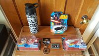 Photo of the full lot showing three Hot Wheels Star Wars die-cast vehicles, a Star Wars badge, and a Stormtrooper-themed water bottle.