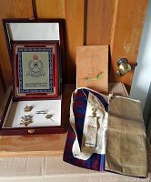 Full lot items including plaque in box, pins, Masonic apron and notebook on wooden surface
