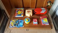 Full view of all Pokemon collectibles on a wooden board including containers, cards, and a Pokemon-themed VHS or DVD case with Pikachu cover