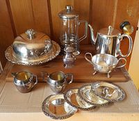 Full lot view including covered serving bowl, sugar and creamer set, silver teapot, cruet, French press coffee maker, and four silver coasters.