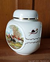 Side views of the white porcelain tea caddy canister with detailed hunting scenes and gold trim on lid.