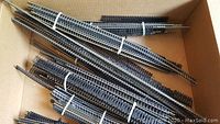 Bundles of straight and curved HO scale model train track pieces tied with white bands and placed inside a cardboard box.