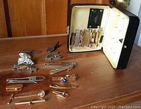 Top view showing assortment of vintage tie pins and clips alongside black travel case open with individual slots inside.