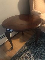 Front angled view of the triangular dark cherry wood occasional table with three drop leaves raised to form a round top, showing the curved legs and polished finish.
