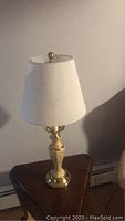 Brass table lamp with marble stem on a triangular wooden side table, showing full lamp with shade.