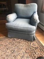 Front angle photo of the light blue overstuffed chair showing quilted upholstery and cushioned armrests on an oriental patterned rug.