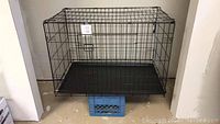 Full view of black metal dog kennel with bottom tray elevated on a crate.