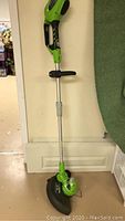 Full vertical view of the Greenworks cordless weed trimmer showing its full length with handle, shaft and cutting head with guard.