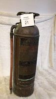 Full view of the vintage copper fire extinguisher showing cylindrical body, top handle ring, and attached hose.