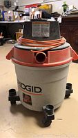 Front view of Rigid wet-dry vacuum showing the hose inlet, power switch, and base with wheels.