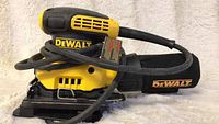 Front and side view of DEWALT quarter sheet palm sander, corded with dust bag attached, cord wrapped around the tool.