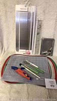 Shows the paper cutter, large and medium silicone mats, metal ruler, orange and blue cutting tool, and several crafting specialty tools laid on the mats.