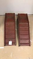 Pair of red steel car ramps side by side on floor, showing full length and ribbed traction surface