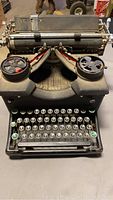 Front view of vintage black typewriter showing keys and ribbon spools