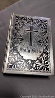 Front cover of the Bible with silver metal cover, cross, and decorative border.