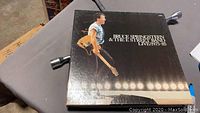 Photo of the outer box cover showing Bruce Springsteen holding a guitar on stage with stage lights below.