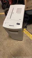 Photo of the Fellowes DM15C paper shredder, showing its front and side view with the brand name and model visible.