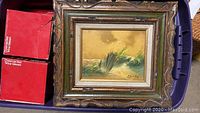 Full view of vintage seascape oil painting in wooden frame, showing waves and grass with yellow sky.