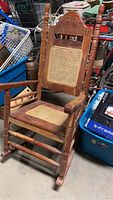 Full view of wooden rocking chair showing caned seat and back with carved decorations