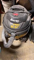 Front view of ShopVac Ultra Pro wet/dry vacuum showing logo, power button, hose attached, and part of the yellow body.