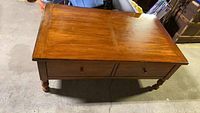 View of the full wooden coffee table showing rectangular top, turned legs, and two drawers underneath.
