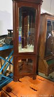 Full front angled view of tall wooden corner curio cabinet with glass doors and metal latches.