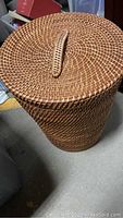 Photo of round woven clothes hamper with lid and handle, showing exterior detail and top view of lid with handle.