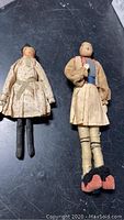 Two early handmade dolls lying on a black surface, showing full body and clothing details.