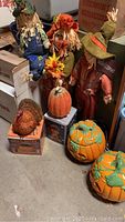 Photo shows three scarecrows with fabric clothing and straw hair, two large ceramic pumpkins, small pumpkin, and glittery turkey on boxes in storage.