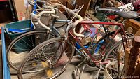 Two vintage road bikes, one blue and one red, stored indoors showing frames, wheels, handlebars, and other components.