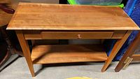 Front view of wooden console table showing top, drawer, legs, and lower shelf