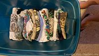 Folded vintage souvenir T-shirts stored in a blue plastic container, showing a variety of designs and colors.