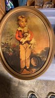 Oval framed vintage print of a boy holding a dog, standing with a hat on ground