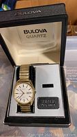 Gold-tone Bulova quartz watch displayed in original box with cream lining and metal Bulova emblem.