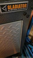 Close-up of Gladiator logo, lock cylinder and diamond plate door panel; grey speckled finish