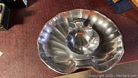 Photo of large shell-shaped metal platter with shiny, reflective surface, ridged shell design.