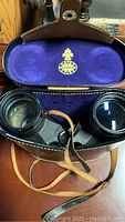 Open leather case showing Tasco binoculars inside with purple velvet lining