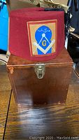 Red fez hat with Free Mason emblem patch, placed on top of wooden storage box