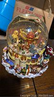 Front side view of the large North Pole themed snow globe showing detailed interior with elves, candy canes, and castle turrets inside the glass globe and detailed base.