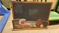 Front view of the large rectangular chalkboard with decorated wooden base featuring hand-painted vintage kitchen items.