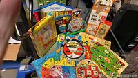 Overview of lot showing multiple children's games and puzzles in bright packaging, including Playskool, Hoo Doo game, and puzzle boards.