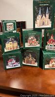 Eight boxed porcelain lighted village buildings arranged showing front views and packaging.