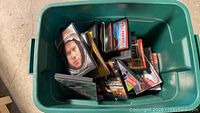 Photo of green plastic bin filled with assorted DVDs including 'Constant Gardener' and 'Mr. Woodcock' visible on top.