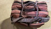 Brown leather carrying bag with multiple zippered compartments, shown closed.