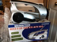 Silver Merriton RD-335AD emergency torch and radio on top of its retail box, showing the crank handle and overall shape.
