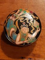 Top view of vintage cloisonne pill box featuring a flower girl design in gold enamel with colorful accents on black background.