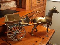 Side view of the brass horse and buggy showing the full length and details of the horse and cart, with the horse's front leg raised.