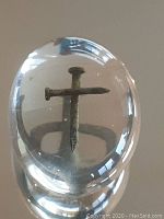 Clear oval talisman approximately 2 inches with rusty nail embedded forming a cross shape