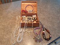Wooden box open showing variety of fashion jewelry inside and jewelry laid out on table around box